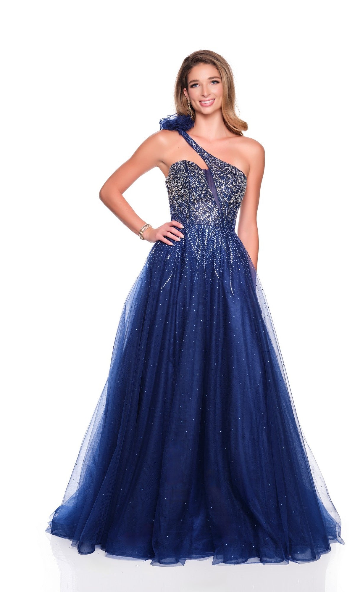 A woman smiles in the Dave and Johnny 12634 long prom dress, featuring a navy blue one-shoulder design with a glitter tulle A-line skirt and sequin embellishments, set against a white background.